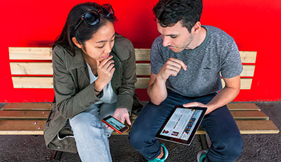 Image of two students looking at an iphone and a tablet.